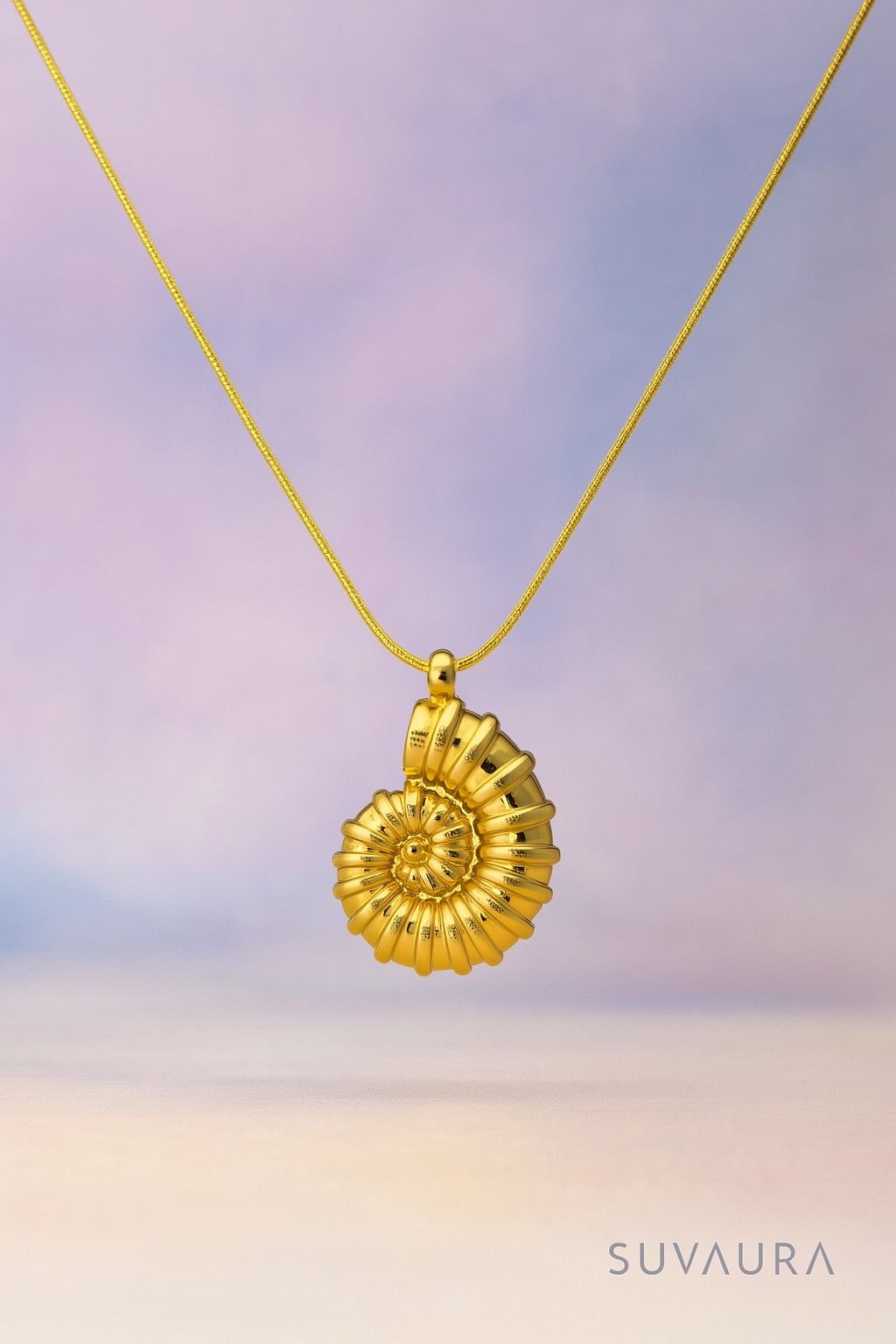 Golden spiral shell pendant necklace with snake chain on soft gradient background – artistic and bold design from Suvaaura