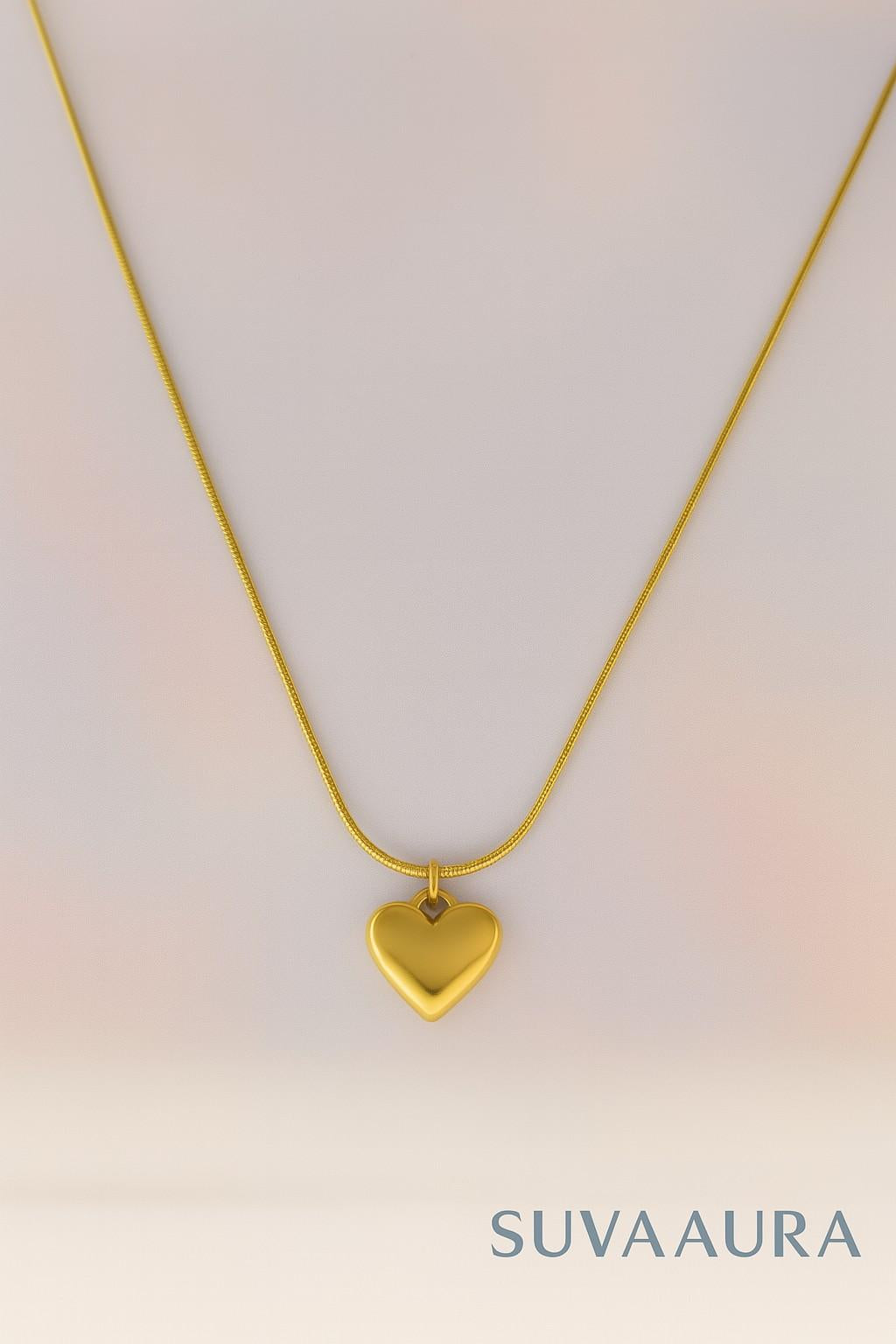 Solid gold heart pendant on sleek snake chain – minimalist love jewellery by Suvaaura on soft pastel background
