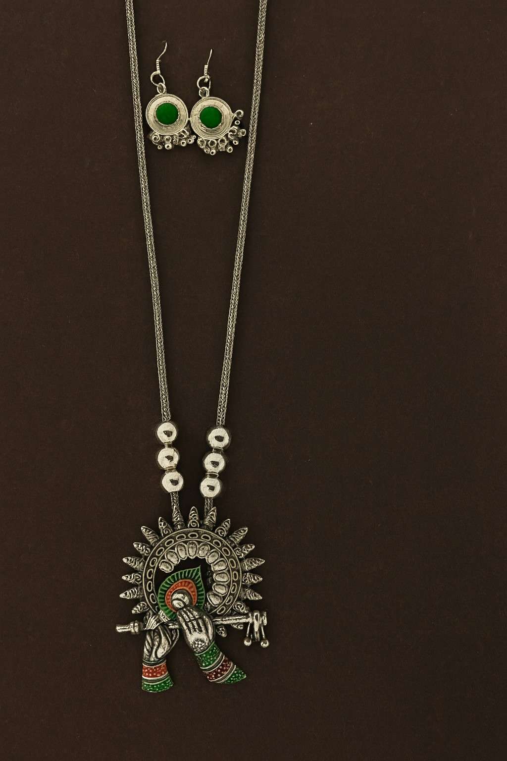 Oxidized Krishna flute pendant necklace set with green stone earrings on brown and beige background – ethnic bohemian tribal jewelry