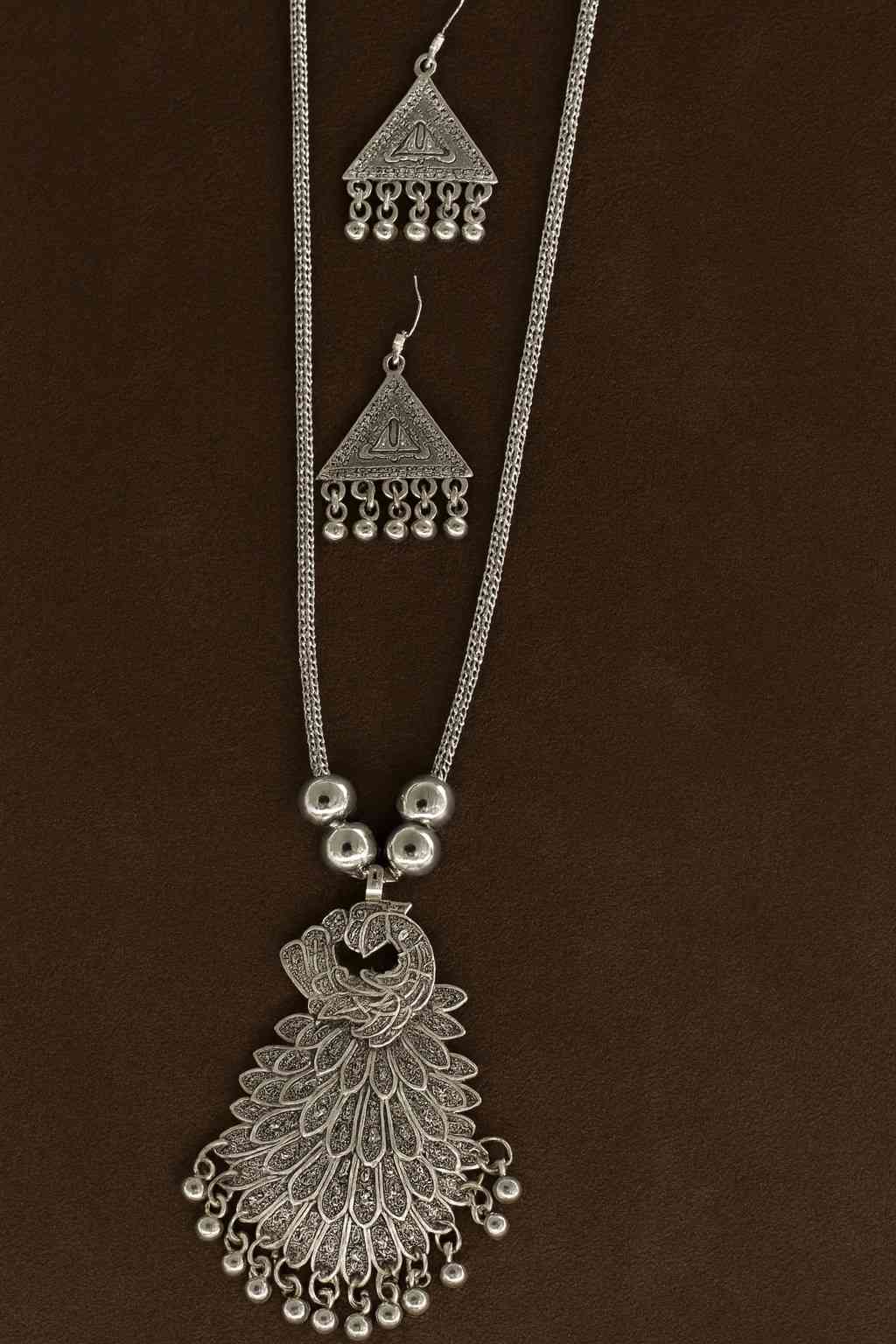 Ethnic oxidized silver peacock pendant necklace with matching earrings on brown background