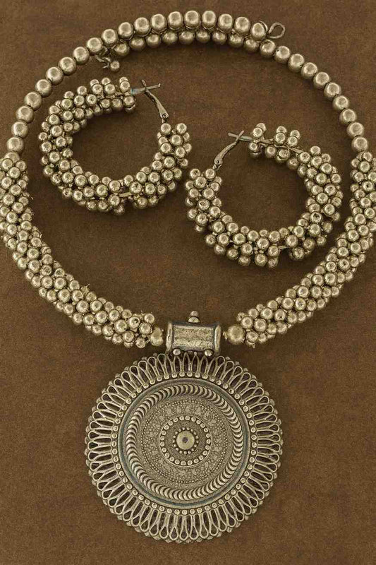 Traditional oxidized beaded choker necklace with engraved pendant and matching hoop earrings on brown background