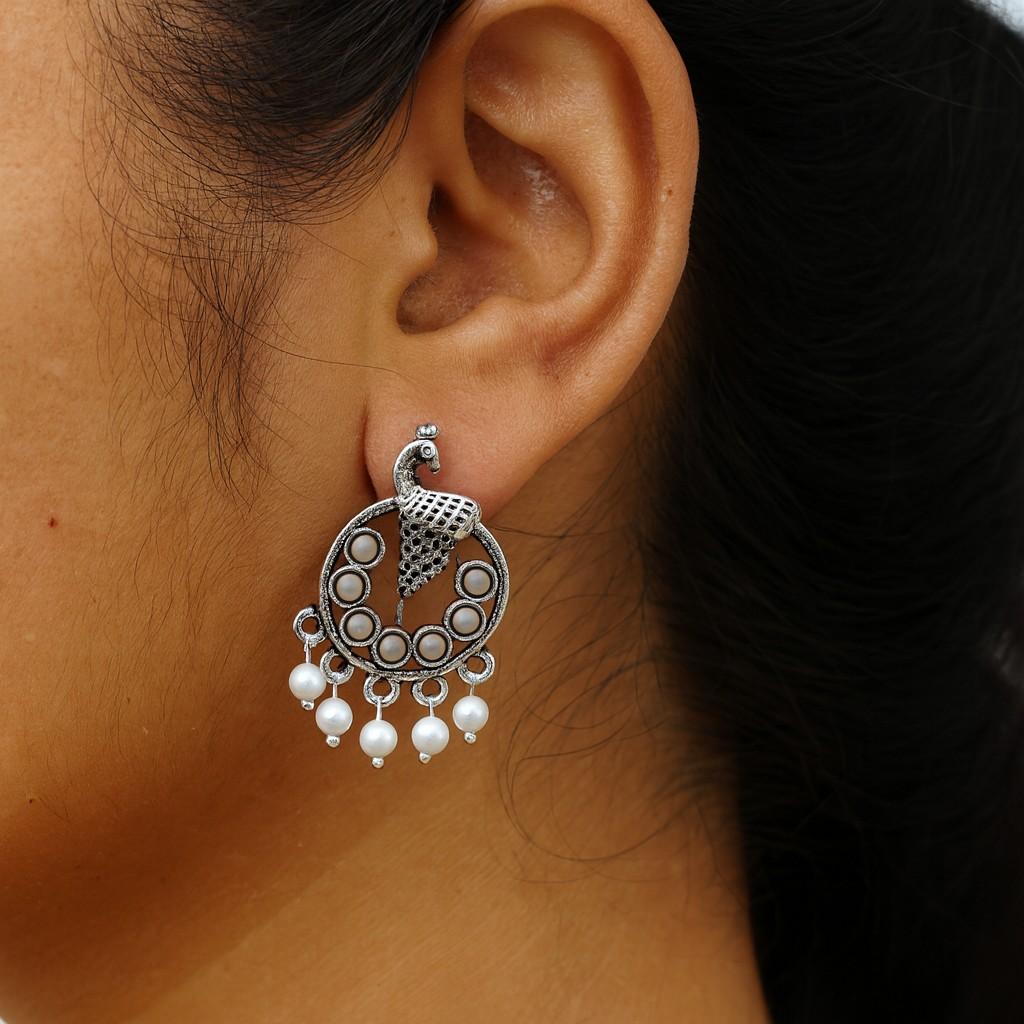 woman wearing antique silver-tone peacock earrings with white bead danglers