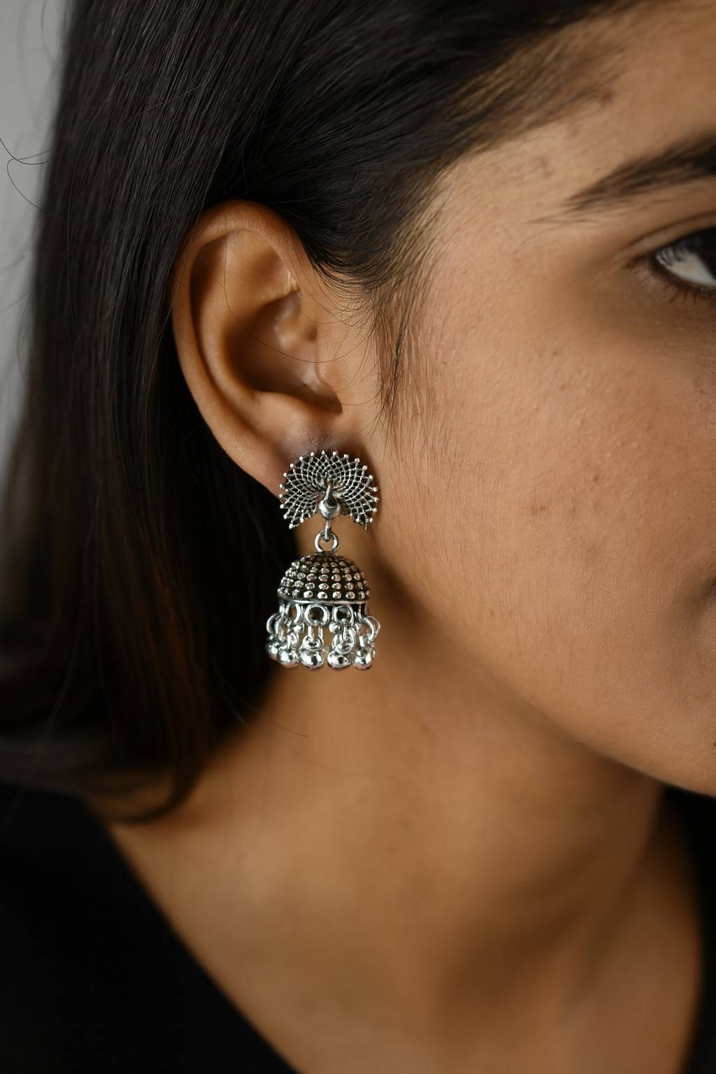 Model wearing oxidized peacock design silver-tone jhumka earrings with hanging beads