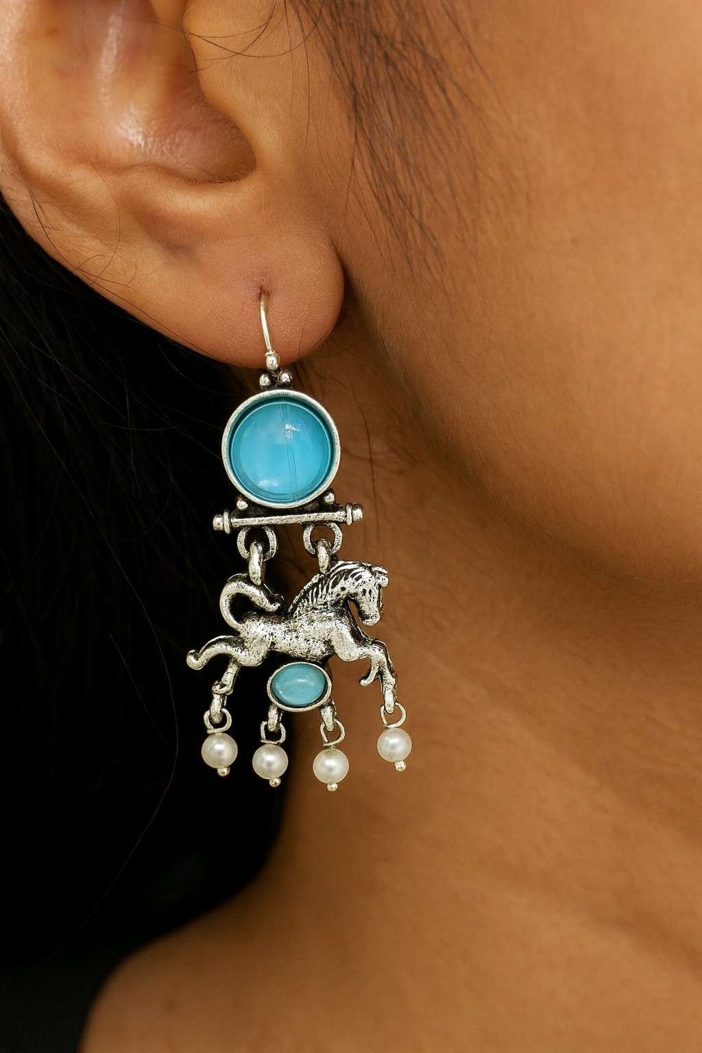 Woman wearing turquoise blue horse design dangle earrings with pearls