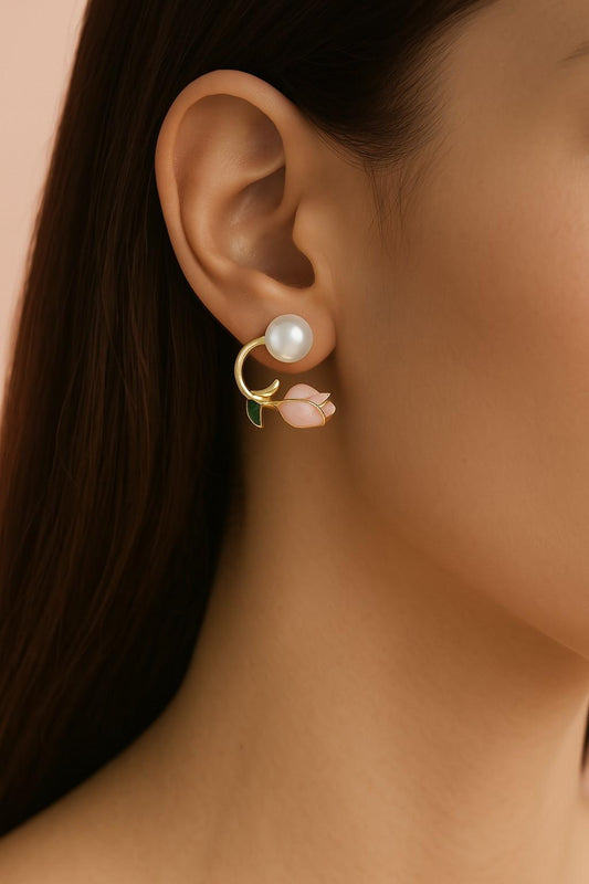 "Model wearing gold-tone pearl stud earrings with pink rose bud floral charm and green enamel leaf detail"