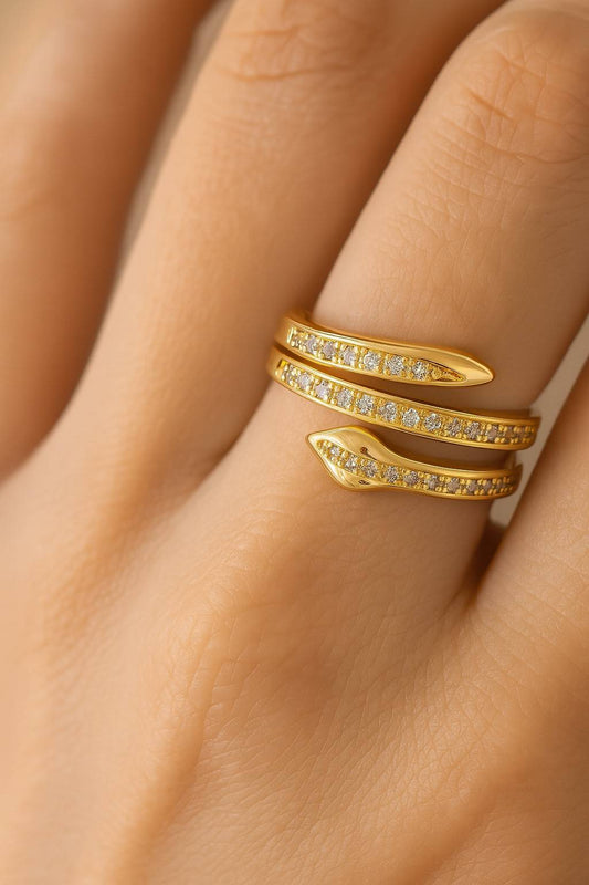 "Gold-tone snake wrap ring with shimmering crystals on pastel background"