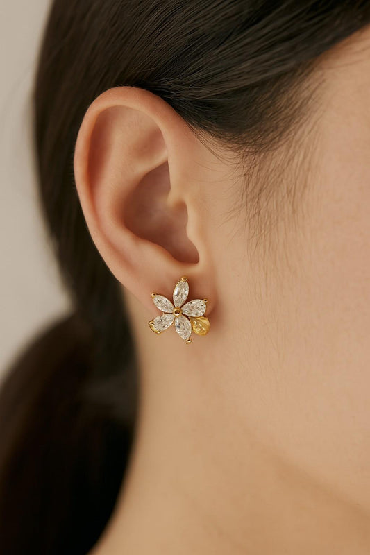 Model wearing gold-tone floral stud earrings with crystal petals and stone base