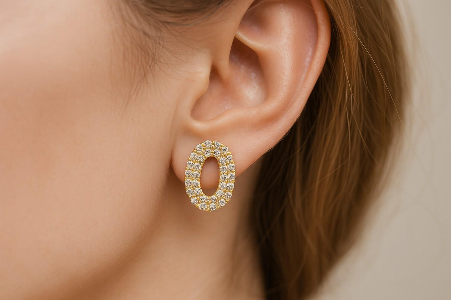 Elegant oval-shaped gold-tone earrings on ear model display