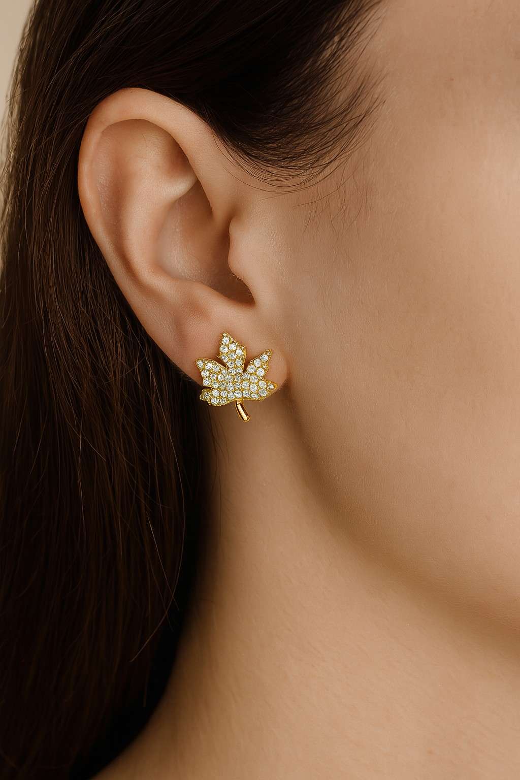 Model wearing golden maple leaf cubic zirconia stud earrings close-up view
