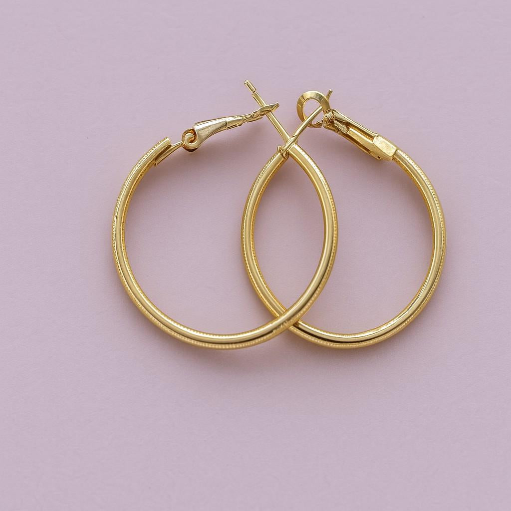 "Classic golden finish hoop earrings on pink background"