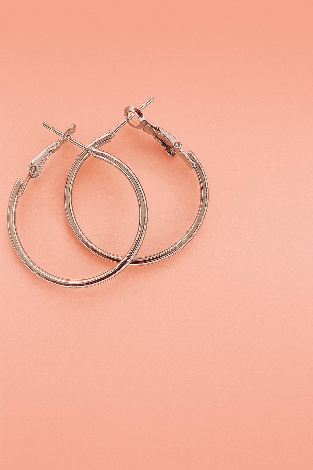 Silver-tone hoop earrings with latch-back closure on peach background