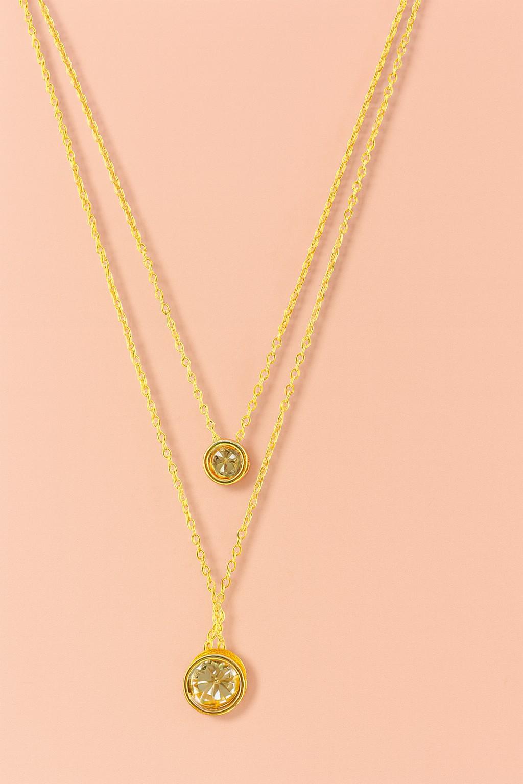 Elegant double layer gold-tone necklace with two round crystal charms on peach background