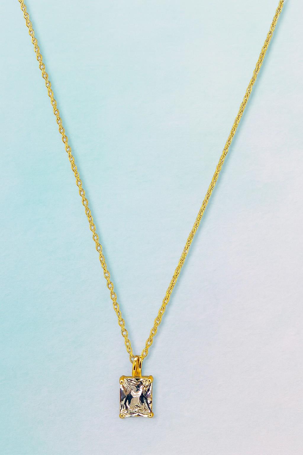 Elegant gold-tone chain necklace with square-cut crystal pendant on blue background