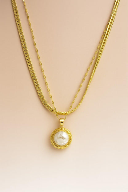 Triple-layer gold-plated necklace with large raw pearl pendant on beige background – perfect for festive and elegant occasions

