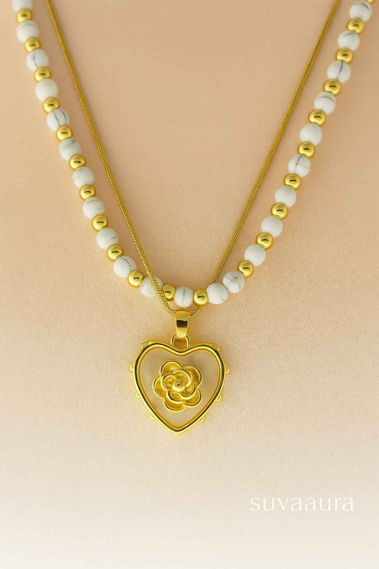 Heart-shaped gold pendant with floral center on dual white and gold bead necklace – Suvaaura romantic jewellery collection

