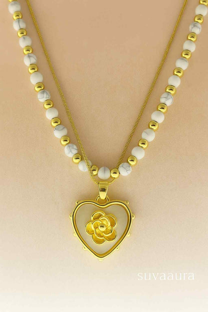 Heart-shaped gold pendant with floral center on dual white and gold bead necklace – Suvaaura romantic jewellery collection

