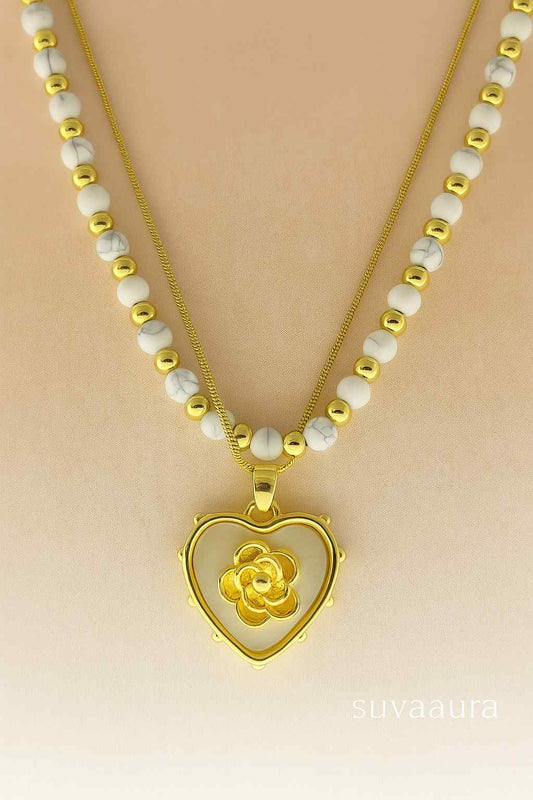 Heart-shaped gold pendant with floral center on dual white and gold bead necklace – Suvaaura romantic jewellery collection

