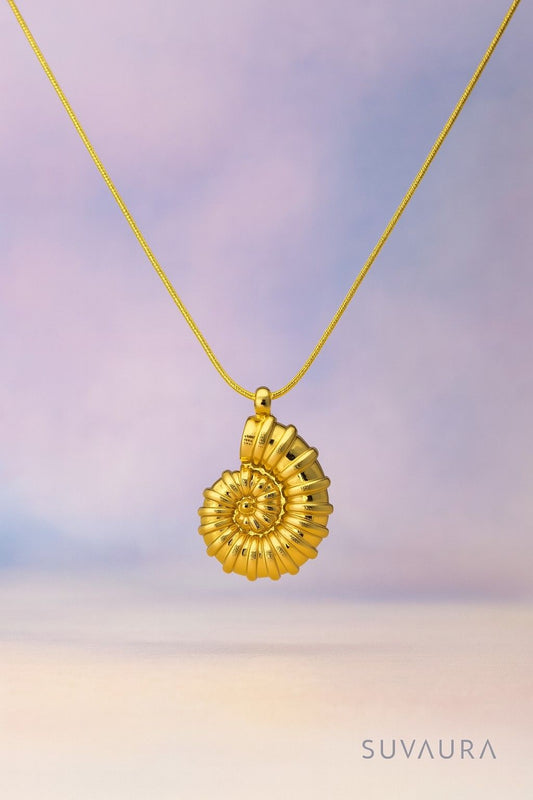 Golden spiral shell pendant necklace with snake chain on soft gradient background – artistic and bold design from Suvaaura

