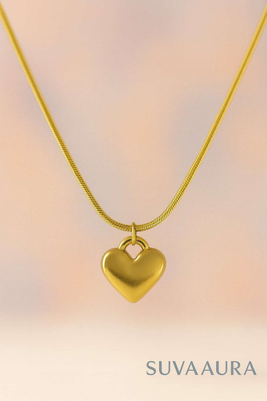 Solid gold heart pendant on sleek snake chain – minimalist love jewellery by Suvaaura on soft pastel background
