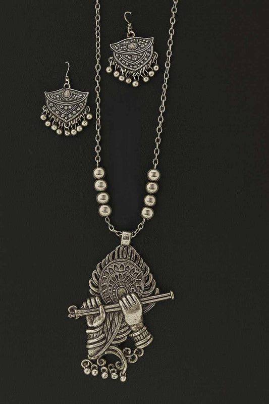 Oxidized Krishna Flute Pendant Necklace Set with matching earrings in antique silver tone on display background.