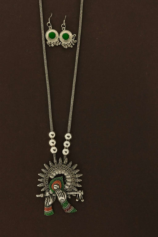 Oxidized Krishna flute pendant necklace set with green stone earrings on brown and beige background – ethnic bohemian tribal jewelry
