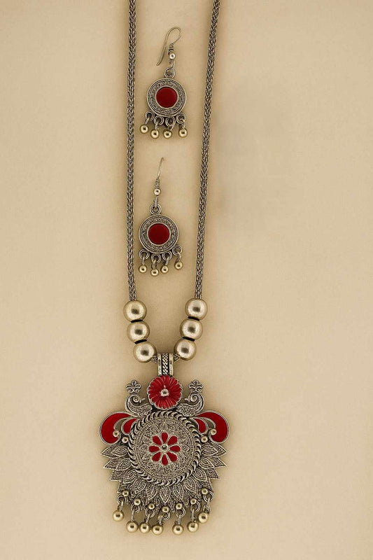 Oxidized silver-tone necklace and earrings set with intricate floral carvings and red enamel detailing, displayed on a neutral background.