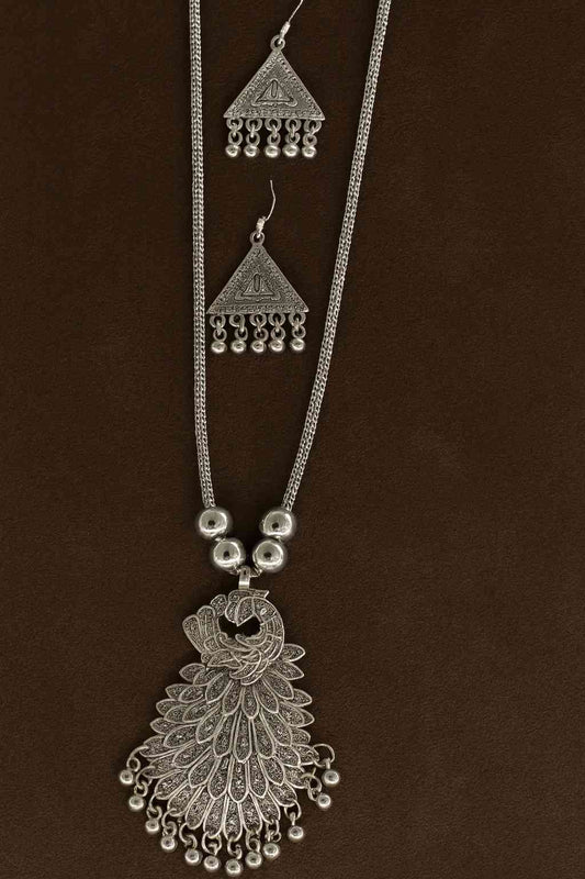 Ethnic oxidized silver peacock pendant necklace with matching earrings on brown background