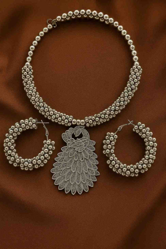 Antique silver-tone peacock choker necklace with beaded hoop earrings on brown background