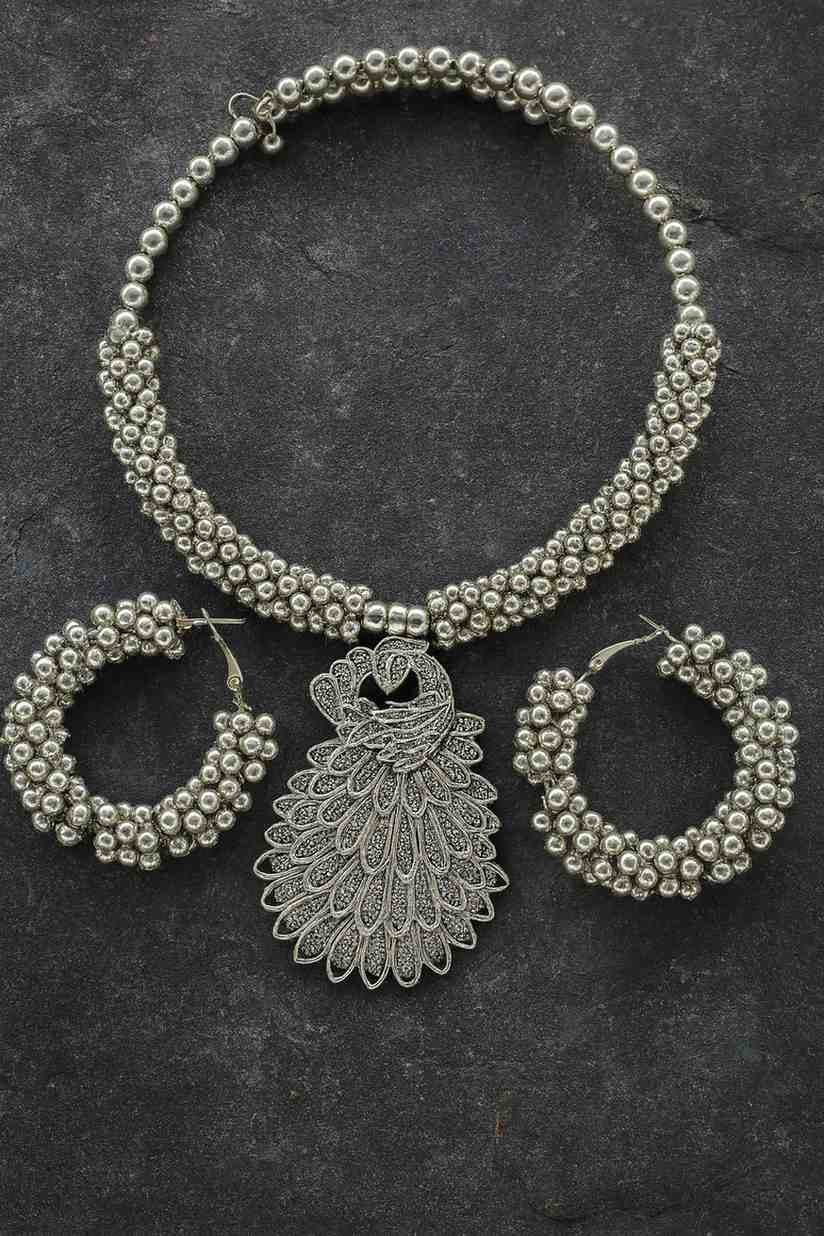 Antique silver-tone peacock choker necklace with beaded hoop earrings on stone texture background

