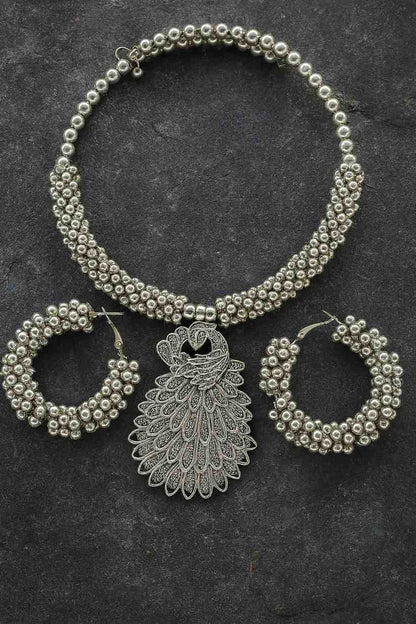 Antique silver-tone peacock choker necklace with beaded hoop earrings on stone texture background

