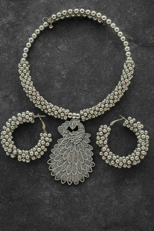Antique silver-tone peacock choker necklace with beaded hoop earrings on stone texture background

