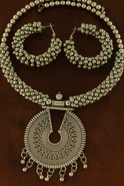Oxidized silver beaded choker necklace set with antique round pendant and matching hoop earrings displayed on brown background