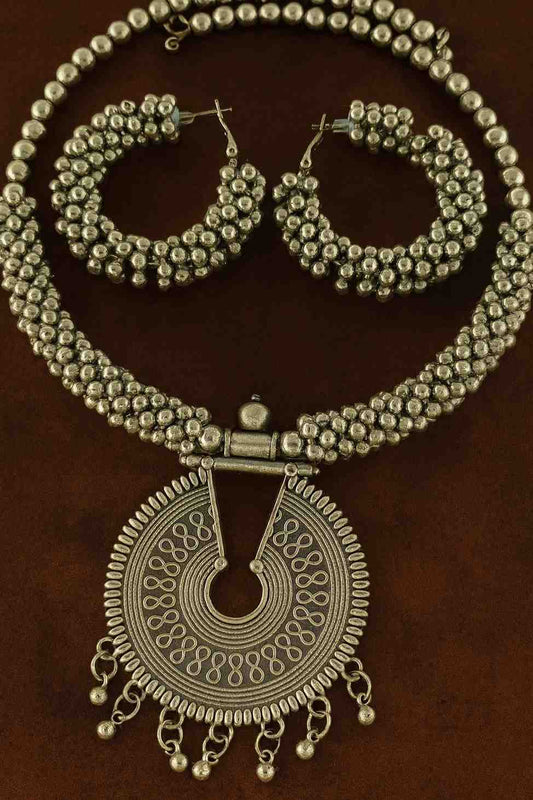 Oxidized silver beaded choker necklace set with antique round pendant and matching hoop earrings displayed on brown background