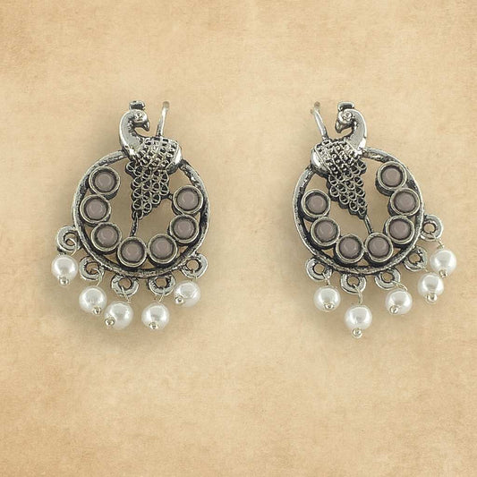 antique silver-tone peacock earrings with white beads on beige background