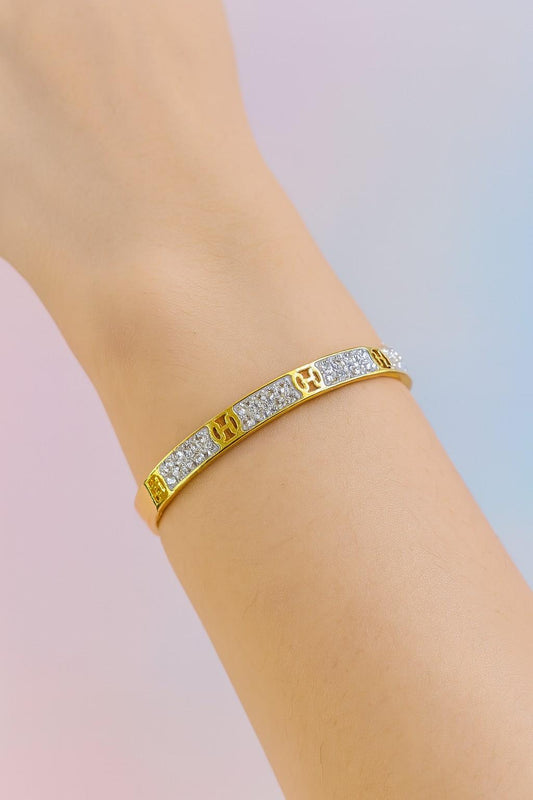 Elegant gold-colored cuff bracelet worn on wrist with sparkling stones