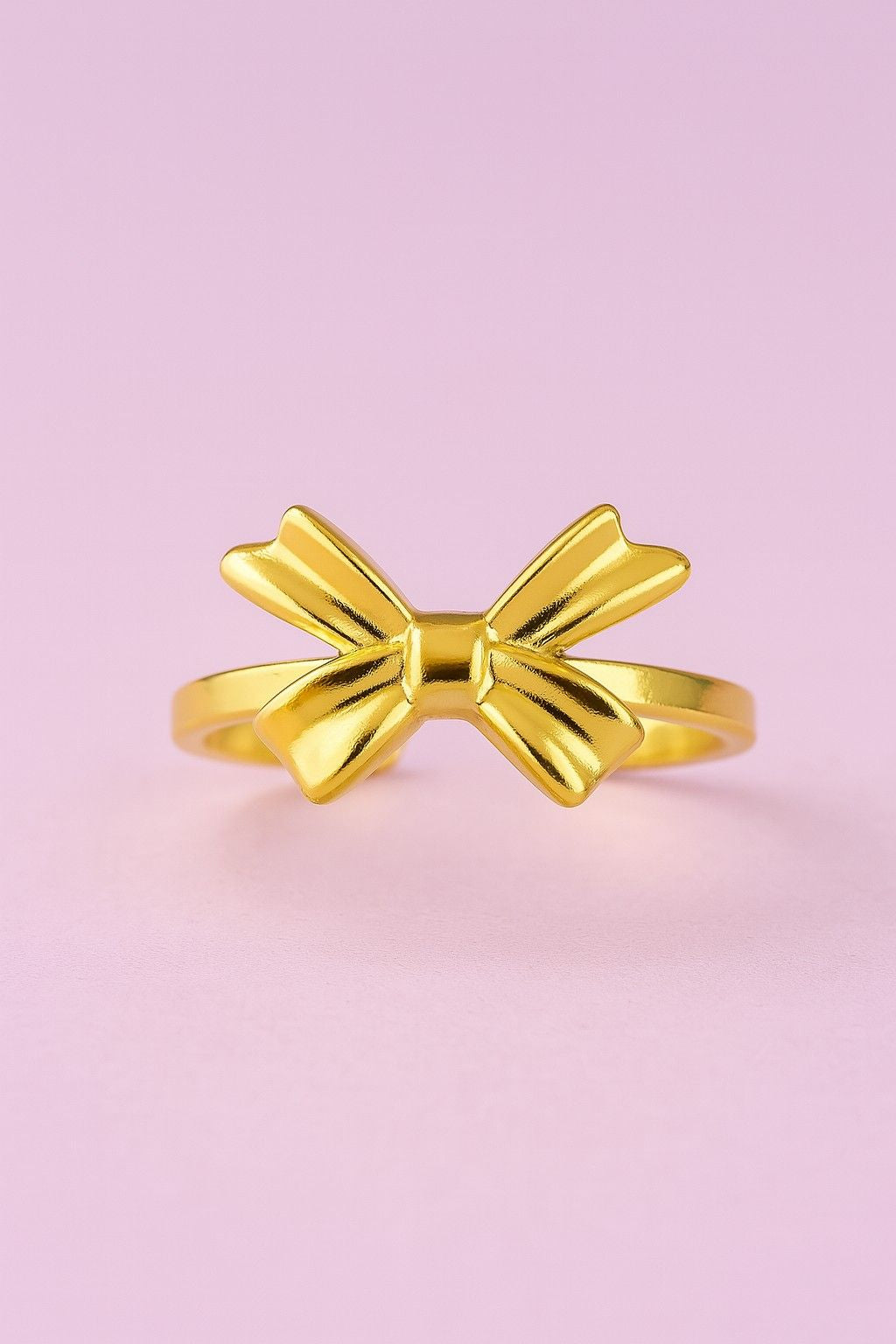 "Minimal gold-tone bow design ring on pastel pink background"