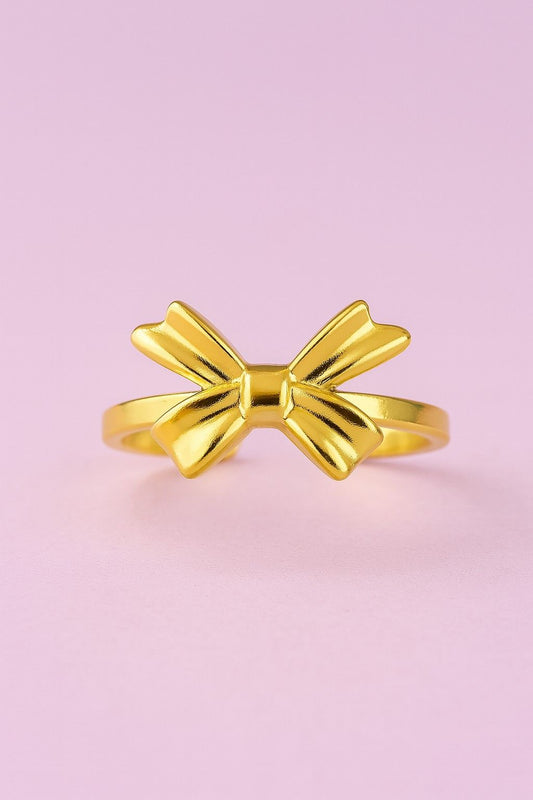 "Minimal gold-tone bow design ring on pastel pink background"