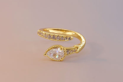 "Gold-tone teardrop stone ring with crystal band on pastel background"