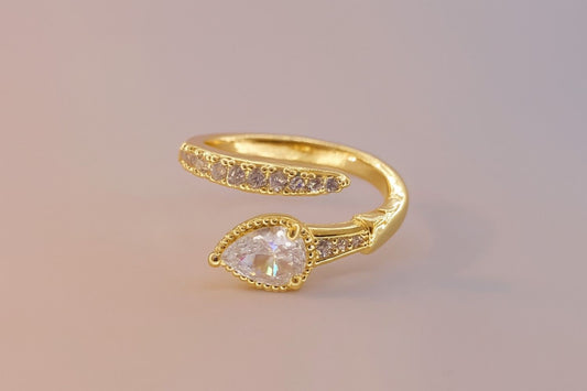 "Gold-tone teardrop stone ring with crystal band on pastel background"