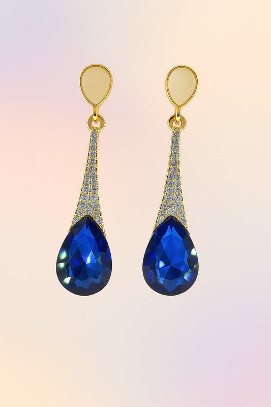 "Elegant golden finish earrings with blue teardrop crystal on soft gradient background"