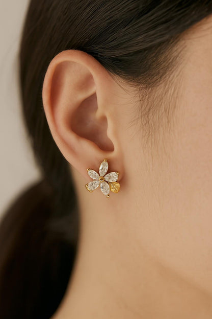Model wearing gold-tone floral stud earrings with crystal petals and stone base

