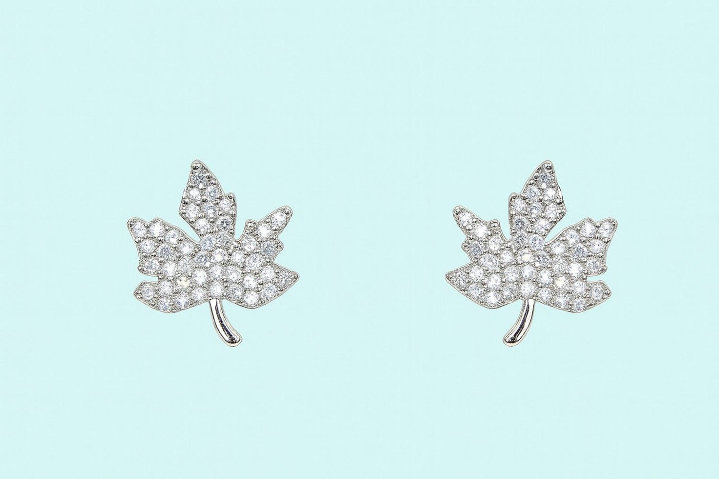 silver-tone maple leaf crystal stud earrings on plain background