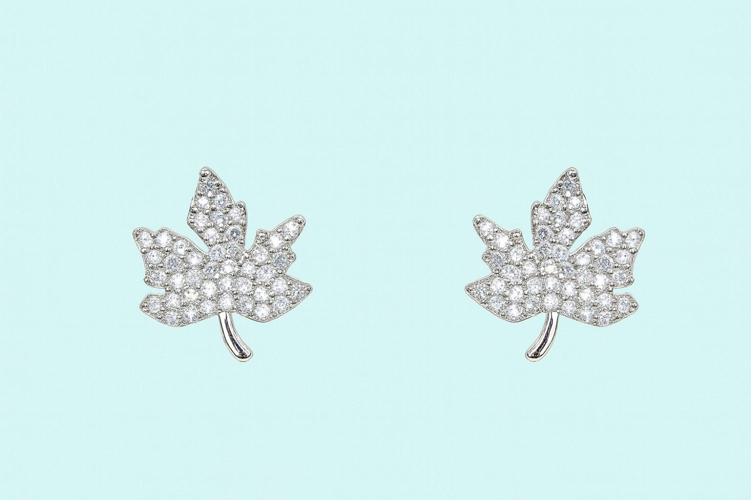 silver-tone maple leaf crystal stud earrings on plain background