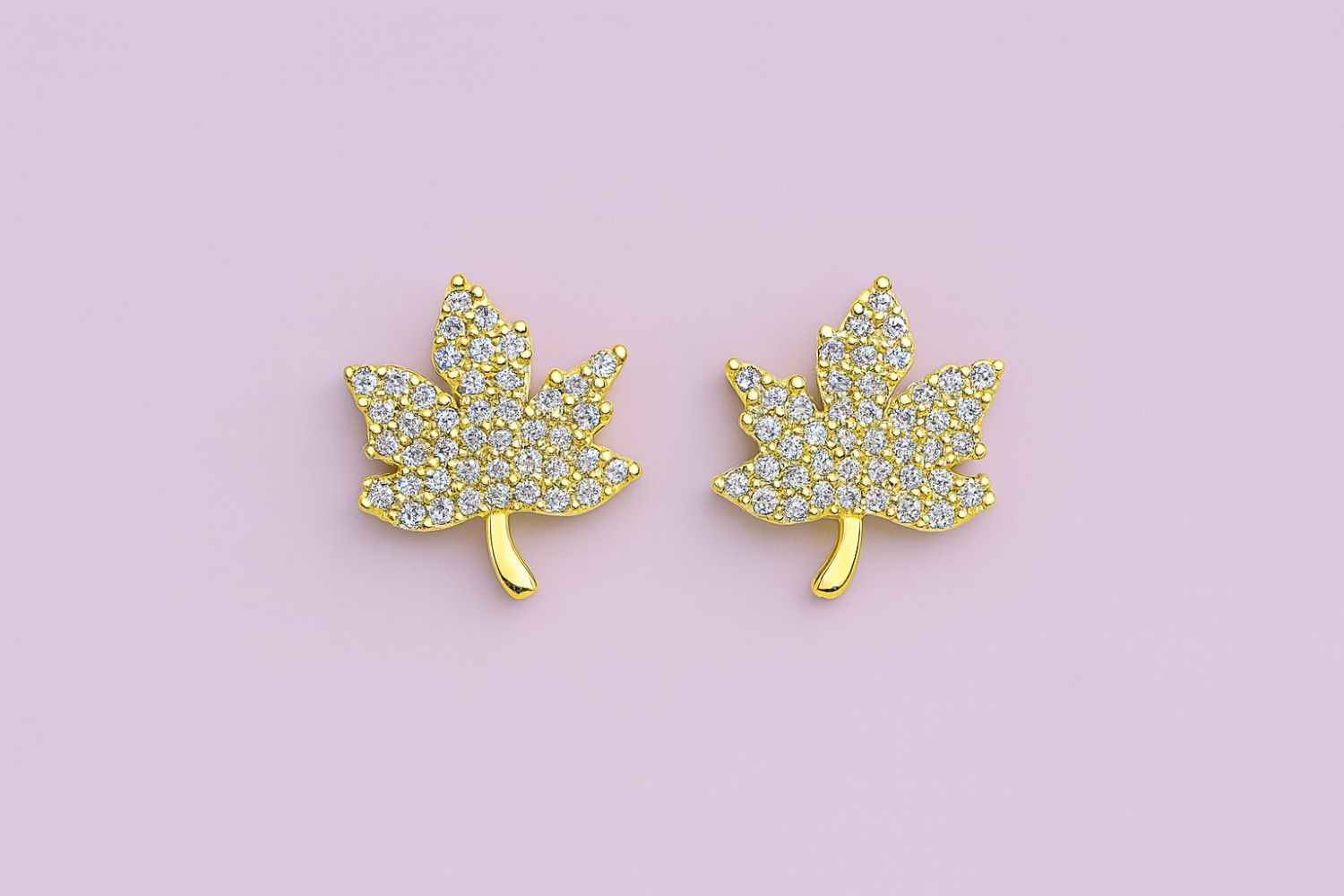 Golden maple leaf stud earrings with sparkling cubic zirconia stones on a pink background