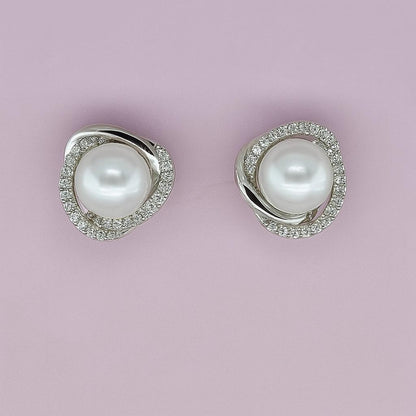 "Silver-tone pearl stud earrings with crystal halo on pink background"