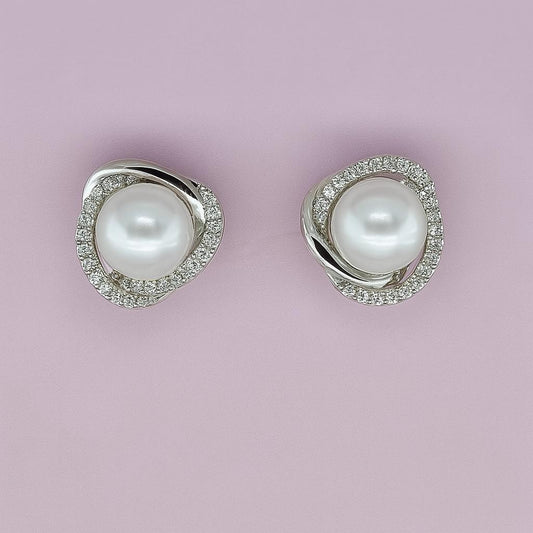 "Silver-tone pearl stud earrings with crystal halo on pink background"