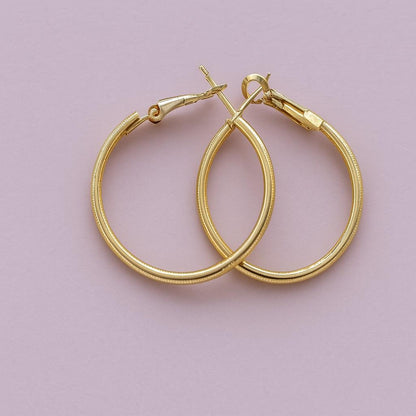 "Classic golden finish hoop earrings on pink background"