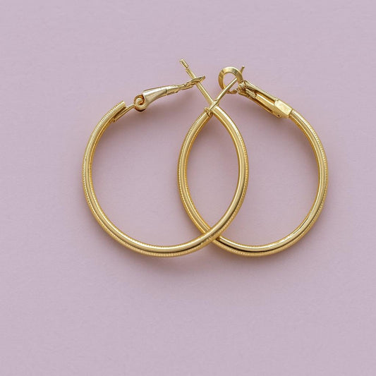 "Classic golden finish hoop earrings on pink background"