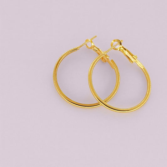 Gold-tone large hoop earrings with latch-back closure on pastel background