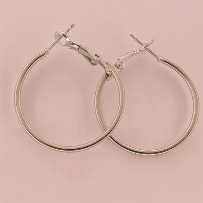 Minimalist silver-tone large hoop earrings on pink background